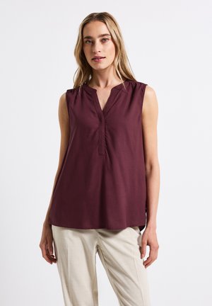 Blusa sin mangas burdeos con escote en V y costuras de hombro fruncidas. Tejido suave con un ajuste relajado, combinada con pantalones beige claros.