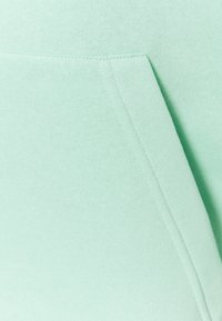 Miętowozielona bluza z gładką fakturą. Posiada przednią kieszeń oraz widoczne przeszycia wzdłuż krawędzi.