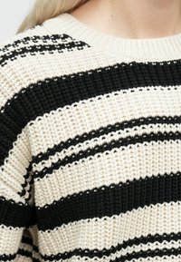 Koor ja mustri triibuline kudum, mida kannab blondide juustega inimene.