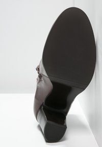 Ruskea nahkainen nilkkuri pyöreällä kärjellä, tekstiilipohjalla ja vetoketjuakennalla. Sileä pinta, jossa on minimaalista ompelua.