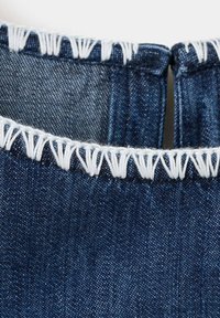 Gros plan sur un tissu en denim bleu avec des bords effilochés et des coutures décoratives blanches le long des ourlets.