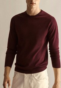 Maglione a maglia bordeaux con maniche lunghe, scollatura a girocollo e polsini a coste. Texture morbida, design aderente, si abbina a pantaloni di colore chiaro.