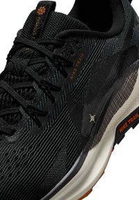 Zapatilla de trail running Nike negra, con un upper de malla texturizada, acentos naranjas contrastantes y una suela duradera con un patrón de tacos.