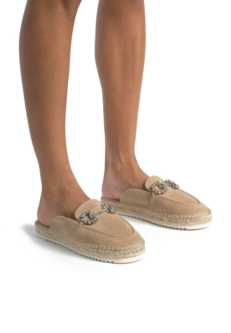 Beige Wildlederschlupfschuhe mit einem Seilsohle, ausgestattet mit Verzierungen aus zwei silbernen Schnallen und einem runden Zehendesign.