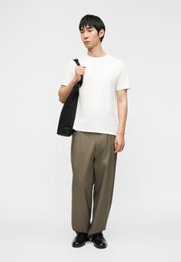 T-shirt blanc en coton associé à un pantalon beige ample et des chaussures en cuir noir. Le mannequin porte un sac fourre-tout en toile noire.