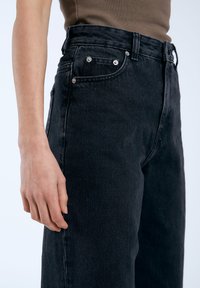 Hoge zwarte denim jeans met vijf zakken, zilverkleurige hardware en een recht gesneden ontwerp. De stof heeft een licht gestructureerde afwerking.