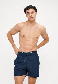Pantaloni da nuoto navy con vita elastica nera che presenta il logo "CALVIN KLEIN". Il tessuto è liscio, leggero e ha una chiusura con coulisse.