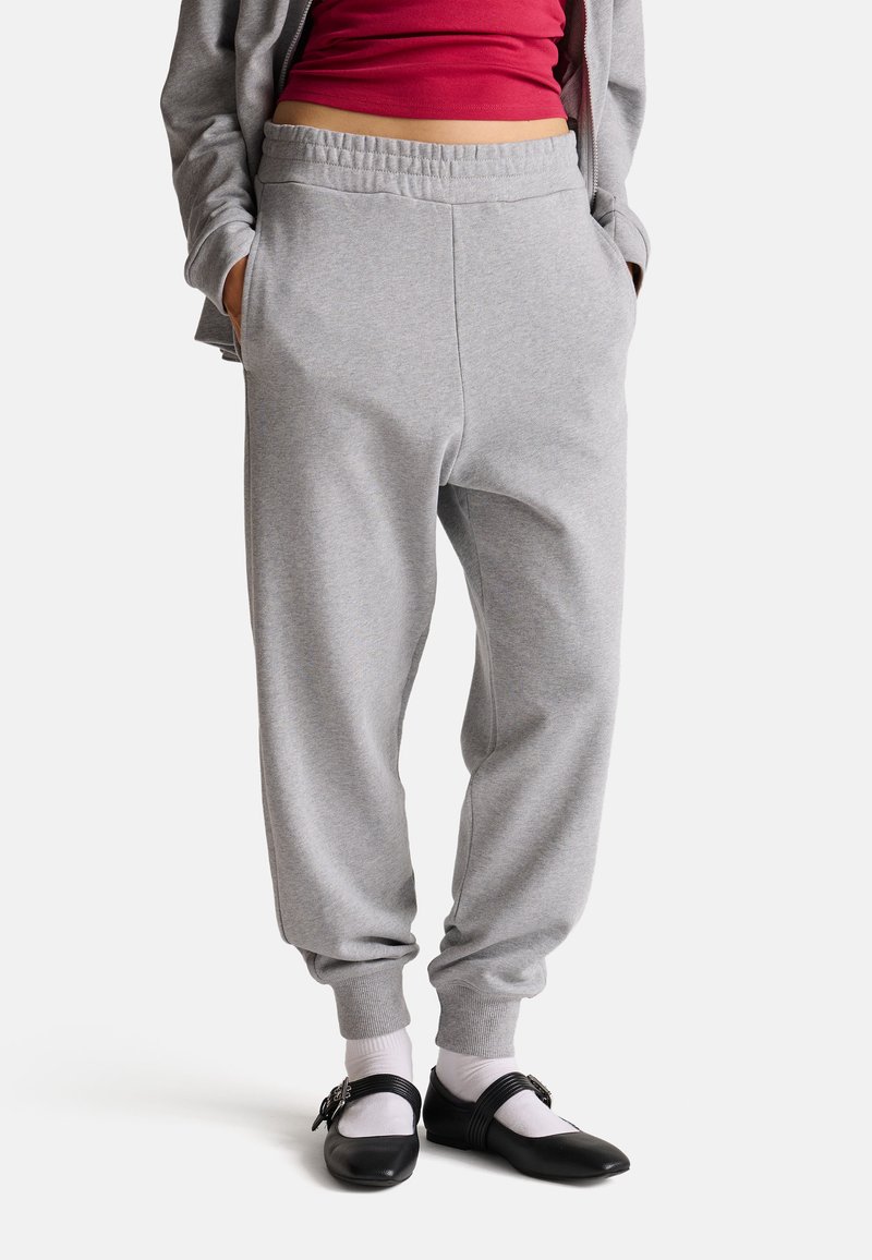 Szare bawełniane dresy z elastycznym pasem, zwężającymi się nogawkami, bocznymi kieszeniami i prążkowanymi mankietami, w zestawieniu z czarnymi balerinami i białymi skarpetkami.