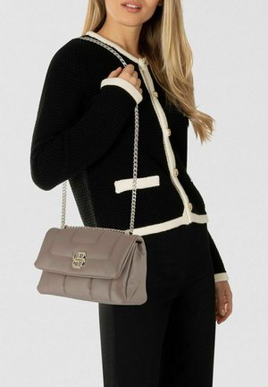 Donna che indossa un cardigan bianco e nero e tiene una borsa trapuntata taupe con tracolla a catena argentata e chiusura con logo sulla spalla.