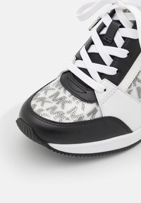 Baskets noir et blanc avec lacets blancs, détails en cuir noir et zone des orteils à motif avec texte gris et sequins.