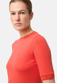 Czerwony top z krótkim rękawem i okrągłym dekoltem. Wykonany z gładkiej tkaniny, o dopasowanym kroju i podwiniętych mankietach. Prosty i nowoczesny design.