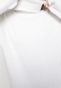 Maglione a collo alto bianco realizzato in un morbido tessuto testurizzato, con un design aderente e colli leggermente sovradimensionati sia sul collo che sui polsi.