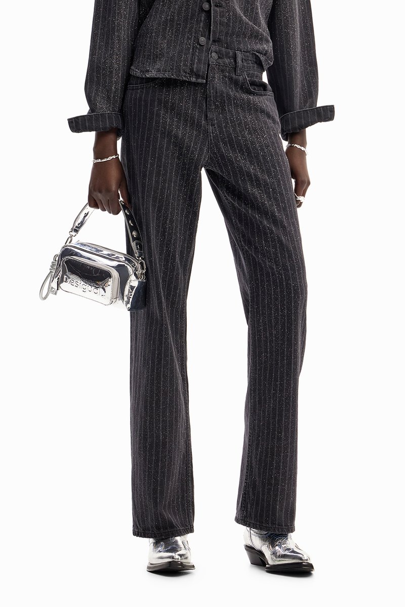 Pantalones de mezclilla negros a rayas con un ajuste ligeramente holgado, combinados con un bolso plateado brillante que presenta acentos de hardware en contraste.