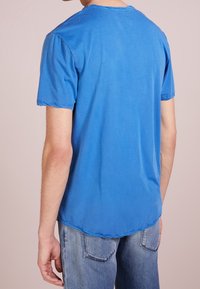 Modré bavlněné tričko s krátkými rukávy, kulatým výstřihem a mírně delším zadním lemem. Minimalistické švy po celém obvodu.