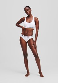 Ensemble de bikini blanc comprenant un soutien-gorge de sport avec une encolure carrée et un slip assorti, tous deux rehaussés d'un texte noir "KARL LAGERFELD".