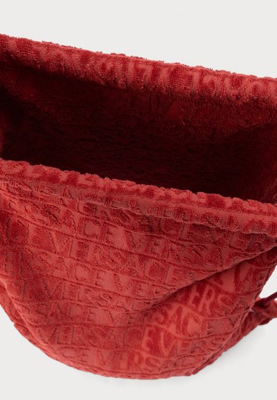 Κόκκινη τσάντα από πετσέτα με ανάγλυφο μοτίβο "VERSACE", απαλή υφή και κλείσιμο με κορδόνι. Ανοικτό πάνω μέρος που αποκαλύπτει την εσωτερική επένδυση.