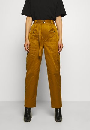 Person wearing mustard high-waist pants with belt, front patch pockets, black top, and black heeled ankle boots against a plain background.