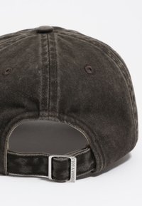 Gorra de béisbol de pana marrón con visera curvada, cierre trasero de metal y detalles de costura a juego. Presenta un botón superior cosido y agujeros de ventilación.