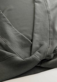 Prim-plan al unui material textile gri închis, pliat, cu cusături vizibile și detalii tricotate texturate, așezat pe o suprafață plană.