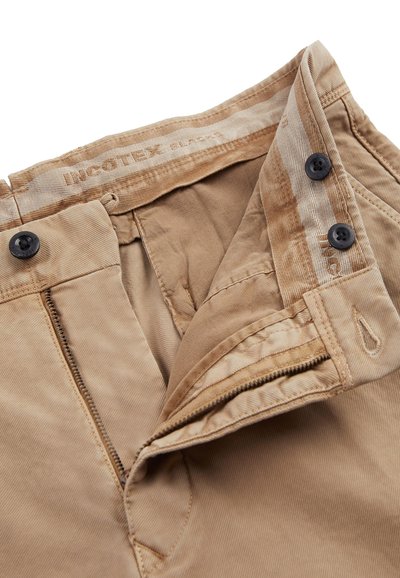 Beżowe spodnie kordowe z zamkiem, dwoma czarnymi guzikami w pasie oraz metką z napisem "nicotex black" na wewnętrznej podszewce.