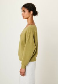 Pull olive green en matière douce et texturée avec une coupe décontractée, des épaules tombantes et un grand col. Présenté avec une jupe gris clair.