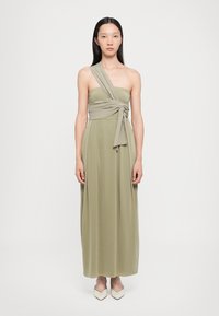 Rochie maxi de culoare verde măsliniu, având un design cu un umăr descoperit și un accent din țesătură răsucită. Textură netedă și siluetă fluidă.