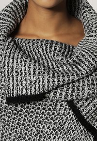 Suéter de punto en negro y gris con un cuello amplio y suelto, que presenta un patrón texturizado y acentos negros contrastantes en los bordes.