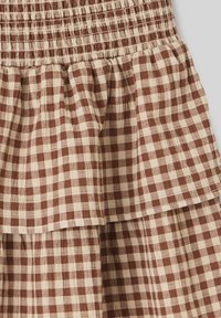 Tissu à carreaux marron et beige avec un waistband élastique froncé et un détail de volant superposé.