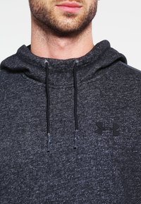 Felpa con cappuccio grigio scuro in tessuto testurizzato, dotata di un cappuccio con lacci e un piccolo logo nero sul petto, che presenta un design casual.