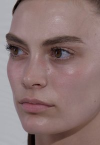 Gros plan d'un visage avec une peau lisse et claire, des lèvres pulpeuses et des sourcils bien définis. Les yeux sont bruns avec de longs cils. Un éclat subtil sur la peau.