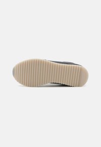 Černé tenisky s texturovaným svrškem, vybavené hladkou, béžovou gumovou podrážkou s horizontálními drážkami pro lepší přilnavost. Viditelné logo značky.