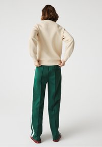 Sudadera crema con cuello redondo y puños de canalé, combinada con pantalones verdes con rayas laterales y detalles de bolsillo trasero.