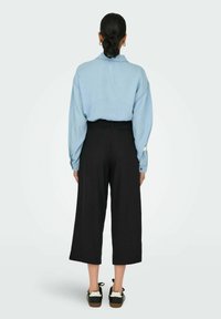 Světle modrá košile s dlouhým rukávem a knoflíky, spárovaná s černými širokými kalhotami. Outfit doplňují černobílé boty s minimálními kovovými detaily.