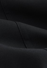 Tessuto nero con una texture liscia, caratterizzato da una lieve lucentezza. Più strati creano profondità e motivi di pieghe, con dettagli di cuciture precise.