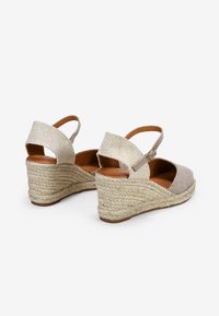 Sandalias de cuña beige con parte superior de tela, tira en el tobillo con hebilla y suela estilo espadrille trenzada. Diseño sin talón.