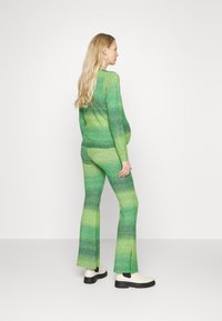Conjunto de suéter e calças de malha em degradê verde, com um design justo, calças com aba e fendas laterais, combinado com botas de tornozelo em creme.