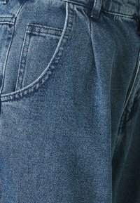 Lähedalt vaadatuna siniste denim-pükste tasku, kus on nähtavad õmblused ja kangatekstuur.
