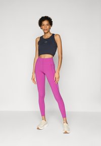 Top crop preto com decote arredondado, combinado com leggings rosa vibrante de cintura alta. Modelo usa tênis atléticos brancos. Textura suave.