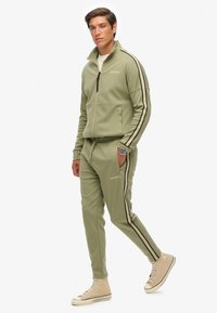 Groene sweatshirt en bijpassende broek van katoenmix, met zwarte zijkanten, ritskraag en logodetail op de borst en dij.