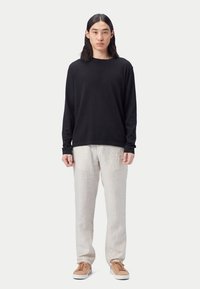 Schwarzes Langarmshirt und beige Leinenhose, kombiniert mit braunen Sneakern. Einfaches Design mit lockerer Passform und weichen Texturen.