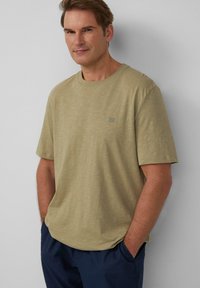 Oliwkowa koszulka z krótkim rękawem, wykonana z miękkiego, teksturowanego materiału, z małym logo na piersi i luźnym krojem.