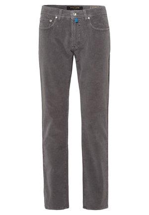 Homme portant un polo à manches longues bleu marine à pois, un pantalon gris coupe slim et des bottes en cuir noir à lacets, debout devant un fond uni.