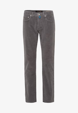 Homme portant un polo à manches longues bleu marine à pois, un pantalon gris coupe slim et des bottes en cuir noir à lacets, debout devant un fond uni.