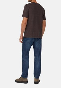 Camiseta de rayas azul marino oscuro, de manga corta y cuello redondo, combinada con jeans de mezclilla azul. Botas de ante marrón. Costuras visibles en los jeans.
