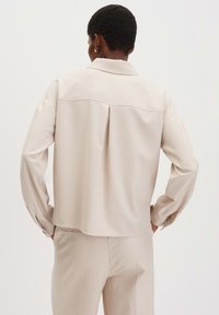 Crème kleurige blouse met een kraag, lange mouwen en een plooidetail aan de achterkant. Gemaakt van een zachte stof met een losse fit.