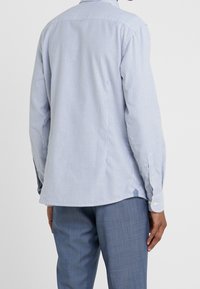 Camicia a maniche lunghe a righe in cotone azzurro chiaro e bianco, con colletto button-down e orlo arrotondato, indossata con pantaloni azzurro chiaro.