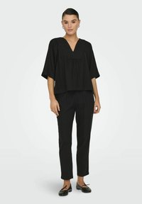 Top cropped nero con scollatura a V e maniche ampie, abbinato a pantaloni neri su misura. Tessuto liscio, design minimalista e scarpe basse.