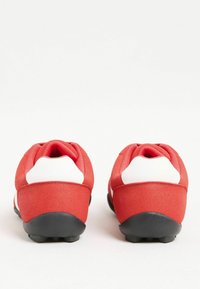 Sarkani zamšas sneakers ar baltām papēža akcentiem un melniem gumijas zolem skatīti no aizmugures uz baltas fona.