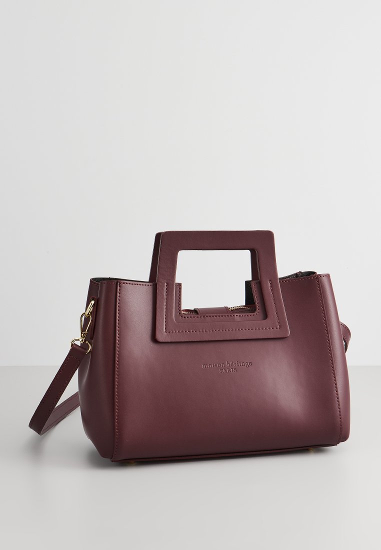 Sac à main en cuir bordeaux avec une poignée supérieure rectangulaire, une bandoulière amovible, des finitions en or et un logo en relief sur le devant.