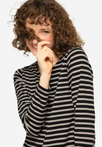 Zwart en crèmekleurig gestreept langslavend shirt met een ronde hals, zachte textuur en een ontspannen pasvorm. Model speelt speels met haar haar.